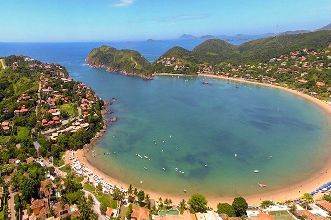 Imagem aérea da Praia da Ferradura, mostrando todas as casas ao redor, a faixa de areia e o mar que dá uma "volta" e chega a parecer um lago.