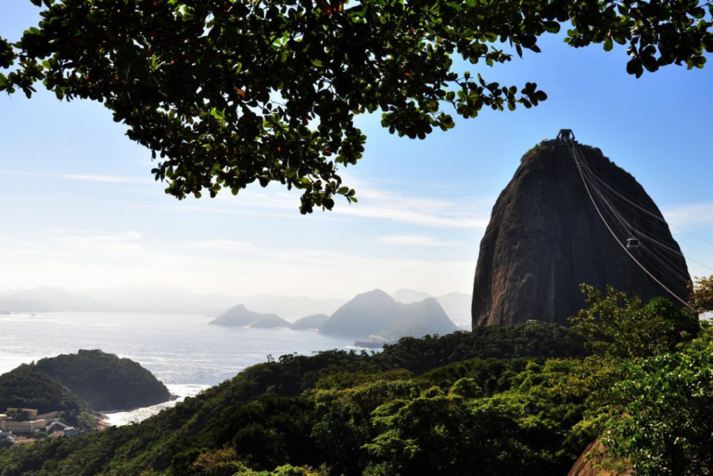 Vista do topo do Morro da Urca, onde é possível ver o Pão de Açúcar, o bondinho a vegetação ao redor e ao fundo, toda a Baía de Guanabara.